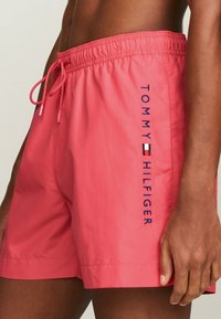 Bañador rosa de tela ligera. Presenta una cintura elástica con cordón y el logo bordado "TOMMY HILFIGER" en el lateral.