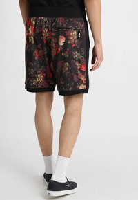 Shorts à imprimé floral noir avec un tissu doux et texturé, une ceinture élastique et une poche arrière zippée pour un rangement sécurisé.