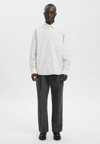 Hvit stripete skjorte med knappelukking, krage, lange ermer og en brystlomme, kombinert med høytlivs grå bukser og svarte sko.