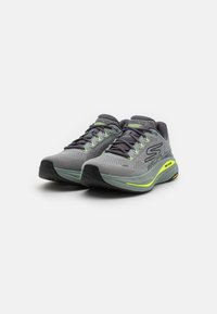 Gray athletic shoes with mesh upper, green accents, and textured sole. Features include lace-up closure and branding on the side.