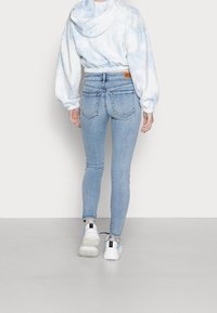 Sudadera azul claro con diseño tie-dye cortada, de dobladillo acanalado, combinada con jeans ajustados de denim claro con cintura alta y dos bolsillos traseros.