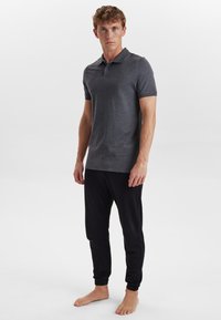 Tmavě šedý polo tričko s krátkými rukávy, v kombinaci s černými jogger kalhotami. Látka vypadá hladce, bez viditelných vzorů nebo log. 