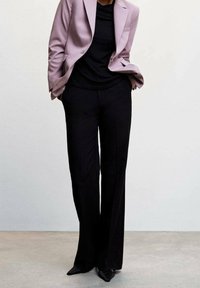 Blazer lilas porté sur un haut noir, associé à un pantalon noir à jambes larges et des chaussures noires à bout pointu. Tissu lisse avec une coupe ajustée.