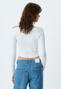 Witte lange mouwen crop top met geribbeld textuur en een off-the-shoulder ontwerp, gecombineerd met lichtblauwe high-waisted denim broek met opgestikte zakken.