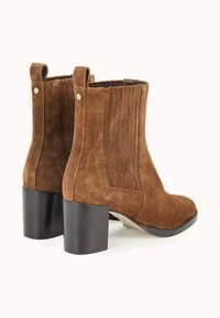 Bottes chelsea en daim marron avec un bout rectangulaire, des détails nervurés sur les côtés et un large talon noir, dotées de tirants à l'arrière.