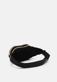 Svart sammet fanny pack med två guld dragkedjor och ett nylonrem. Den har en mjuk textur och en kompakt, rektangulär form.