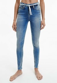 Jeans skinny de mezclilla azul deslavada con cintura ajustable y bolsillos frontales. Presentan una textura suave y un corte ajustado.