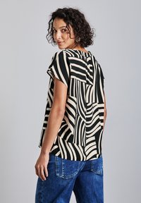 Blusa a righe nere e crema dal taglio rilassato, con maniche corte e schiena aperta. Abbinata a pantaloni in denim blu. Tessuto liscio.