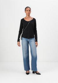 Svart langermet topp med rund hals, blå vid bukse og svarte spisse hæler. Inkluderer en sølvfarget kjetting crossbody-veske.
