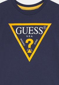 Marineblaues Baumwoll-T-Shirt mit einem gelben, dreieckigen Logo, das "GUESS", "U.S.A." und den Text "WASHED JEANS" zeigt, sowie einem zentralen Fragezeichen-Motiv.