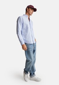 Svetle modrá košile s dlouhým rukávem a knoflíkovým límcem, zkombinovaná se svetle modrými džíny a bílými teniskami. Tmavá čepice s logem. Neformální vzhled.