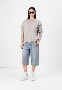 Grå hettegenser med ribbestrikkede mansjetter, løstsittende lyseblå denimshorts og hvite sneakers med grå sokker. Sorte solbriller fullfører stilen.