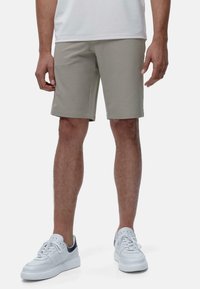 Shorts gris clair en tissu lisse, coupe ajustée, avec des lignes épurées et un ourlet droit. Associés à des baskets blanches avec des accents bleu marine.