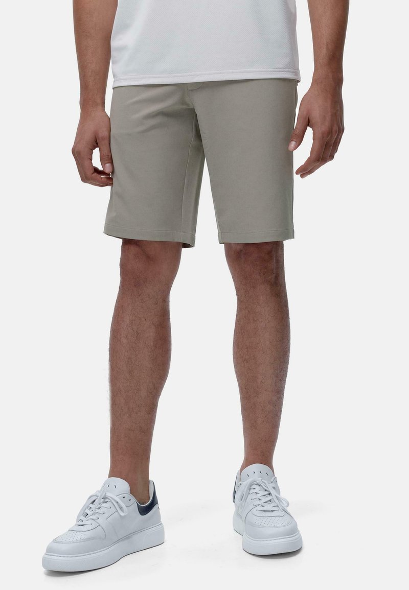 Shorts gris clair en tissu lisse, coupe ajustée, avec des lignes épurées et un ourlet droit. Associés à des baskets blanches avec des accents bleu marine.