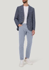 Marineblauw gestructureerd blazer, wit T-shirt, lichtblauwe chinos en witte sneakers. Blazer heeft twee knopen, chinos met zakken, casual fit.
