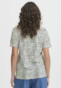 T-shirt a maniche corte di un beige chiaro con un motivo a stampa di leopardo nero. Tessuto morbido, vestibilità standard e scollatura arrotondata.