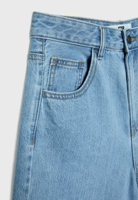 Jean en denim bleu clair montrant la partie avant supérieure avec passants de ceinture, poche avant, petite poche pour pièces de monnaie et fermeture par bouton.