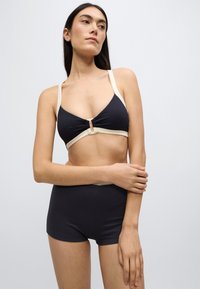 Μαύρο ριμπ τοπ μπικίνι με μπεζ τιράντες, με λεπτομέρεια κλειδώματος και ταυτόχρονες ψηλόμεσες σλιπ σε απαλό ύφασμα.