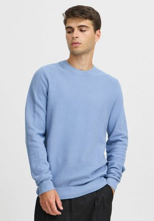 Hellblau strukturierter Strickpullover mit Rundhalsausschnitt und gerippten Bündchen, kombiniert mit dunklen Hosen. Glatte Stoffoberfläche, lockere Passform.