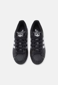 Czarne trampki z białymi paskami, teksturowanym gumowym noskiem i czarnymi sznurówkami. Logo marki znajduje się na prostokątnej metce na języku.