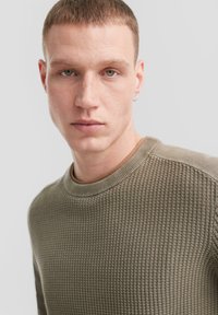 Olivgrüner strukturierter Pullover mit ribbeligem Rundhalsausschnitt und passenden Bündchen. Verfügt über ein Waffelstrickmuster und ein minimalistisches Design.