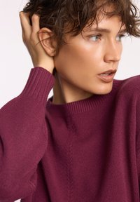 Malinowy sweter z dzianiny z okrągłym dekoltem i długimi rękawami. Miękka tekstura z delikatnym wzorem wzdłuż szwu na ramieniu.