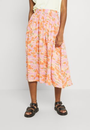 Bloemrijke midi-rok in roze, oranje en groene tinten met plooien. Gekleed met zwarte sandalen met banden en gespen.