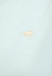 Light blue short-sleeve shirt made of soft fabric featuring a small beige embroidered horse logo on the left chest area.