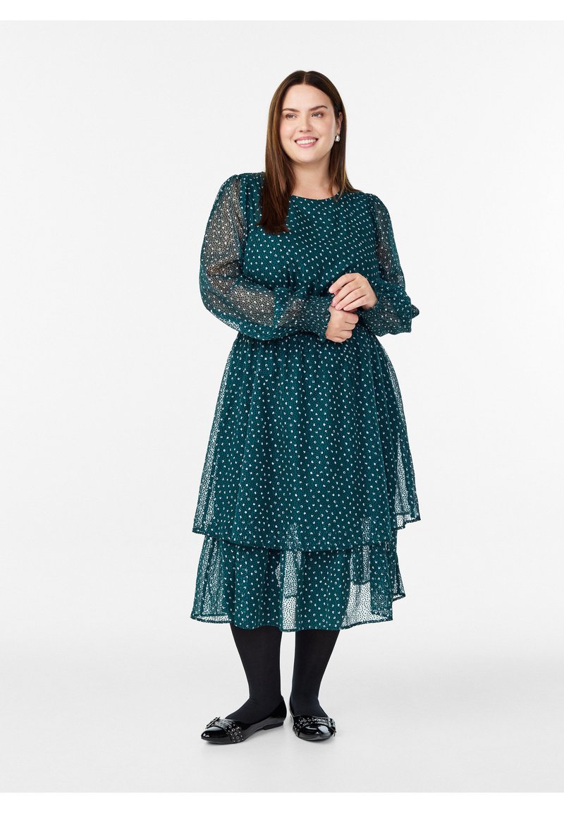 Tiffany oblek s točkicama u boji tirkizne sa prozirnim dugim rukavima i slojevitom suknjom. Uparena s crnim tajicama i sjajnim crnim balerinama s detaljima mašne.