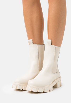 Bottines en cuir blanc avec une semelle épaisse, dotées de panneaux latéraux élastiques et de languettes pour un enfilage facile. Texture lisse et design à bout arrondi.