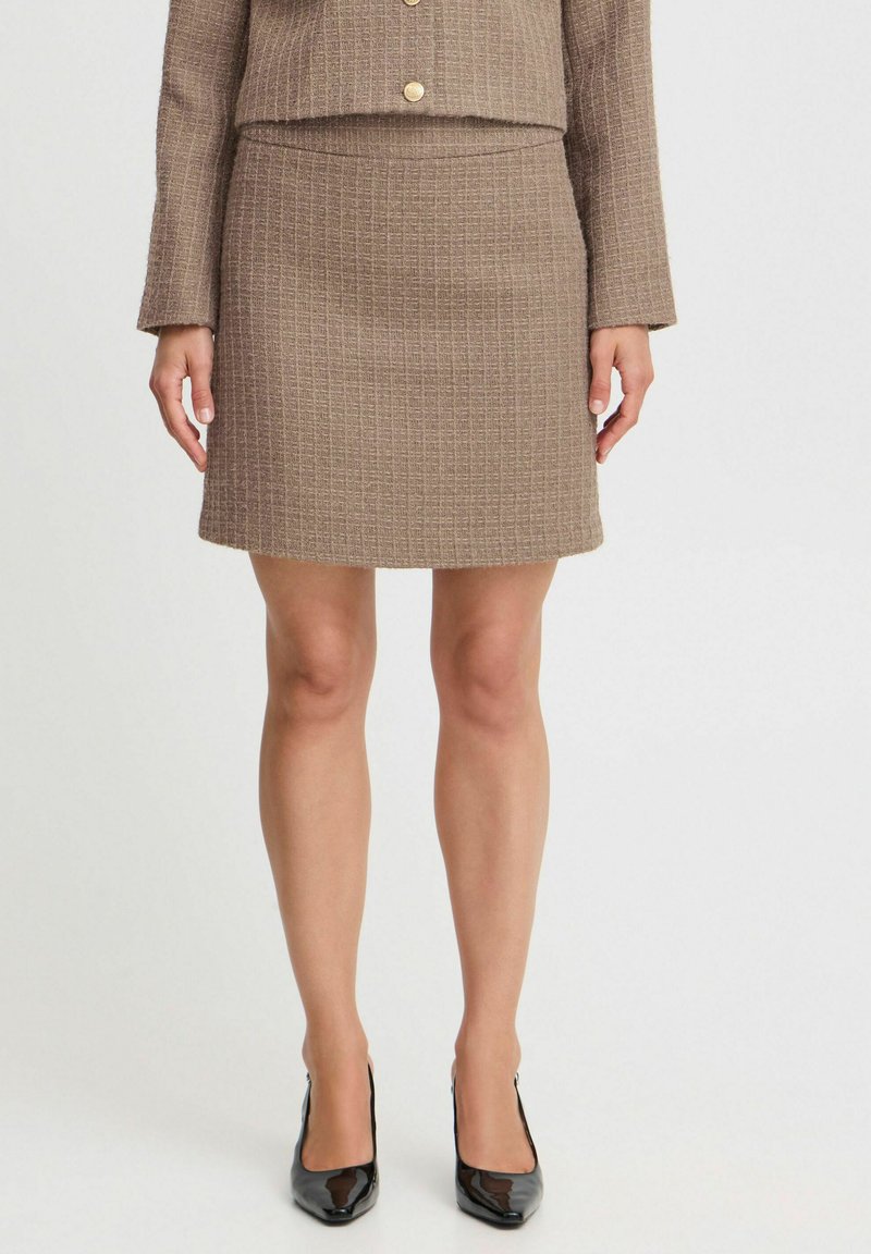 Bruin geweven twee-delig kostuum met een gestructureerde cropped blazer met gouden knoopsluitingen en een bijpassende aansluitende rok. Zwarte hoge hakken.