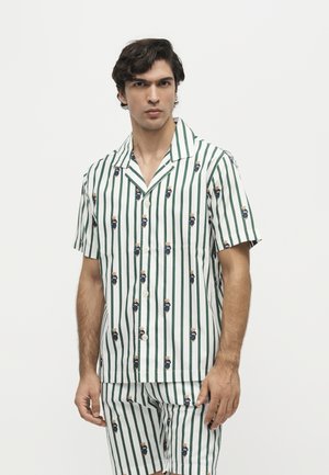 Man wearing white short-sleeve button shirt and matching shorts with green vertical stripes and small teddy bear prints.