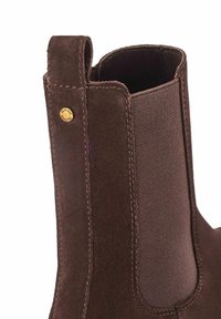 Brązowy zamszowy botek za kostkę z elastycznym panelem bocznym, wzmocnionymi szwami i metalowym logo na pięcie, co ułatwia zakładanie.