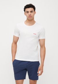 T-shirt blanc à col rond en coton léger avec le logo rouge "HUGO", associé à un short bleu foncé en tissu doux et texturé.
