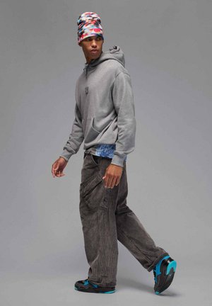 Szara bluza z kapturem z przednią kieszenią, pod nią niebieska koszula z wzorem, ciemne spodnie bojówki z bocznymi kieszeniami oraz czarne trampki z turkusowymi akcentami.