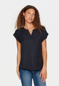 Blusa navy con scollo a V e maniche corte, realizzata in tessuto leggero con un sottile motivo a pois. Vestibilità casual, perfetta per essere indossata a strati.