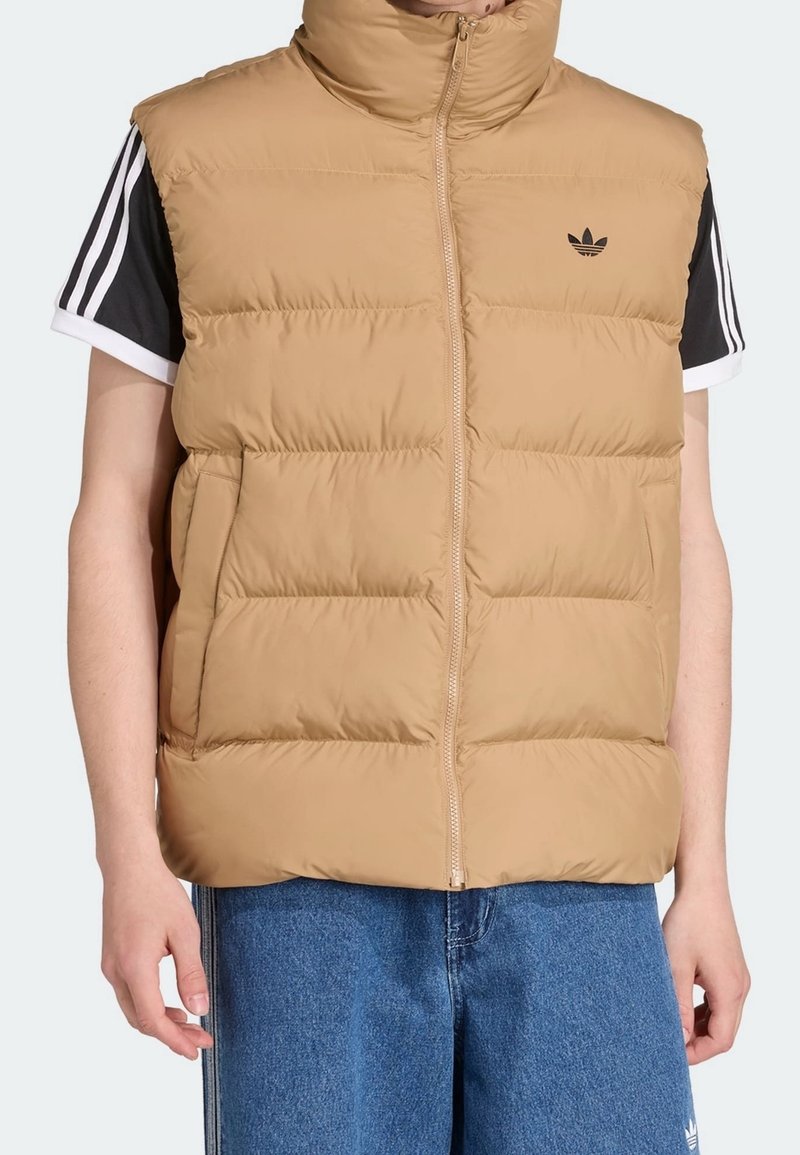 Světlohnědá prošívaná vesta s vysokým límcem, předním zipem a dvěma bočními kapsami. Na prsou má černé logo a prošívaný design.