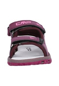 Lila sandal med justerbara velcroremmar, platt sula och en strukturerad fotbädd. Har en logotyp på remmen och kontrasterande rosa detaljer.