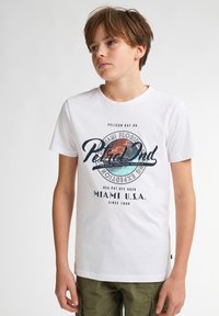 Camiseta de algodón blanca con un gráfico colorido que muestra el texto "Pelican Bay Dr." y "Miami U.S.A" en azul marino y turquesa. Mangas cortas y cuello redondo.