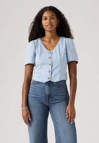 Lichtblauw cropped denim shirt met korte pofmouwen, voorzien van een V-hals en vijf knopen aan de voorkant. Gekocht in combinatie met high-waisted blauwe jeans.
