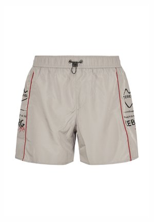 Light beige men's swim shorts with elastic waist, black drawstring, red side piping, and black and red logo text on sides.