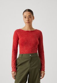 Langemouwig, rood katoenen top met een zachte, gestructureerde afwerking en geschulpte manchetten, gecombineerd met olijfgroene cargobroek met zijzakken.