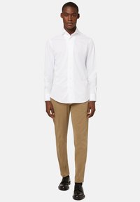 Witte langemouwhemd met knoopsluiting aan de voorkant, gecombineerd met lichtbruine chino's en zwarte schoenen. Glad weefsel, getailleerde fit en puntige kraag.