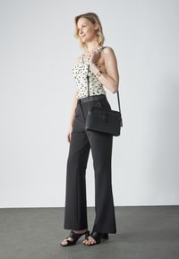 Schwarze gewebte Handtasche mit Klappenverschluss und Schultergurt, kombiniert mit einem weißen Oberteil mit schwarzen Polka-Dots und weit geschnittenen schwarzen Hosen.