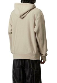 Sudadera con capucha beige de corte relajado, que incluye un bolsillo tipo canguro y puños acanalados. Combinada con pantalones negros a rayas.