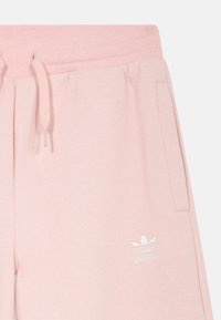 Svetloružové bavlnené tepláky s elastickým pásom, šnúrkou na stiahnutie, bočnými vreckami a malým bielym logom Adidas na prednej strane.