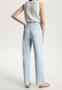 Jeans de tiro alto en azul claro con pierna recta, dobladillo ligeramente deshilachado y dos bolsillos traseros, combinados con un top sin mangas de punto blanco.