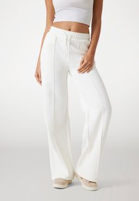 Witte wijde broek met een elastische tailleband, trekkoordsluiting en zijzakken. Gladde textuur, minimalistisch ontwerp, geen patronen.