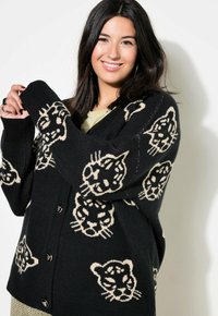 Musta neuletakki, jossa on leopardikuosi kermanvärisenä, nappikiinnitys edessä ja ribattu hihansuu. Pehmeä materiaali, rento istuvuus ja ylimääräinen muotoilu.