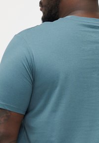 Short-sleeve, crew-neck t-shirt in muted teal cotton. Smooth texture with a relaxed fit, displaying shoulder seam details.